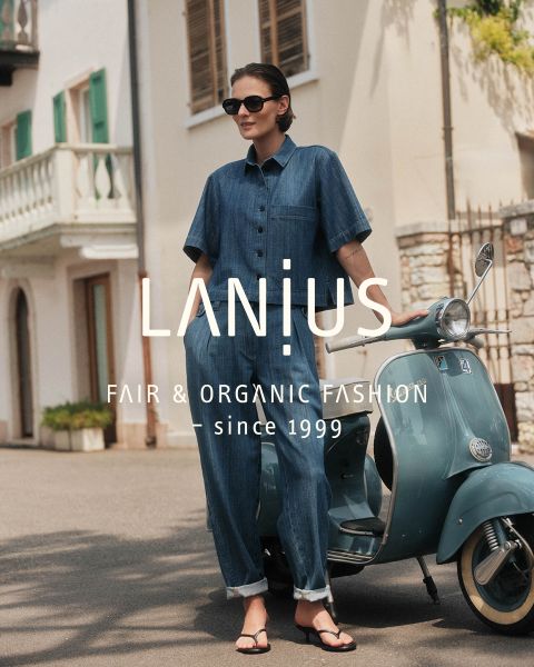 Une femme dans une longue robe bleu foncé est assise entre des formations rocheuses stratifiées. Le texte superposé se lit comme suit : "LANIUS FAIR & ORGANIC FASHION - depuis 1999.