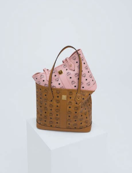 Une femme portant une veste en peau de mouton retournée marron clair, un short noir et des bottes se tient sur une marche en pierre et tient un grand sac. En arrière-plan, un homme en vêtements colorés semble flotter horizontalement au-dessus des marches. Derrière eux, on peut voir des arbres.