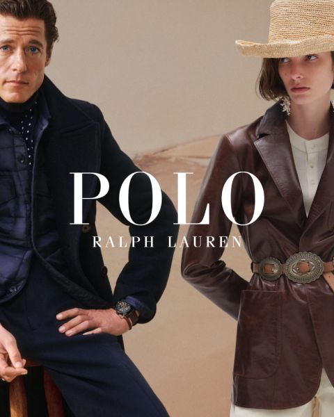 Un homme et une femme portent d'élégants trench-coats Ralph Lauren. L'homme associe son manteau à un pull coloré et un pantalon gris, tandis que la femme porte une chemise rayée, des gants marron et une large ceinture. "POLO RALPH LAUREN" est affiché en lettres blanches.