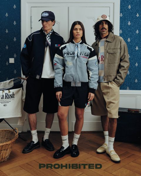 Deux hommes sont assis sur une terrasse en bois dans les hautes herbes et jouent au backgammon. L'un porte un bonnet rouge, une chemise à carreaux et un jean, l'autre un bonnet marron, une veste olive et un pantalon foncé. Au-dessus d'eux, il est écrit « INTERDIT ».