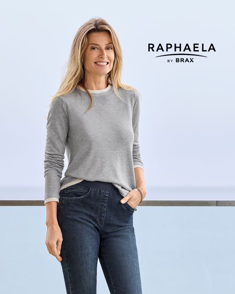 Une femme aux longs cheveux blonds, portant une chemise grise à manches longues et un jean foncé, se tient souriante près d'une balustrade avec un fond bleu clair. À côté d'elle apparaît le texte "EUREX by BRAX".