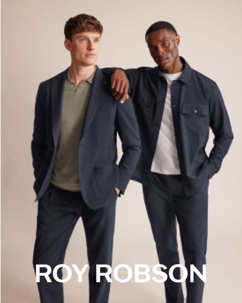 Un homme se tient à l'extérieur devant des montagnes enneigées, portant un manteau pied-de-poule gris, un pull gris et un pantalon gris. Le texte "ROY ROBSON" apparaît en bas de l'image.