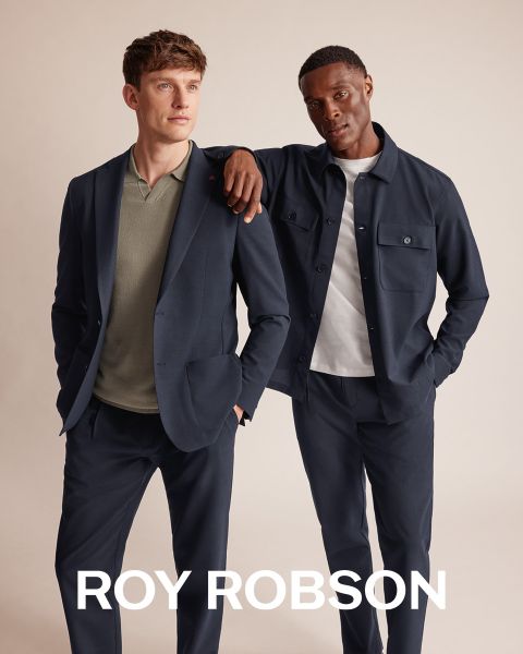 Un homme se tient à l'extérieur devant des montagnes enneigées, portant un manteau pied-de-poule gris, un pull gris et un pantalon gris. Le texte "ROY ROBSON" apparaît en bas de l'image.