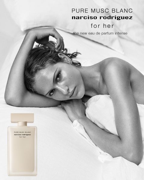 Une femme aux cheveux bruns bouclés pose de profil à côté d'un flacon de parfum rose portant l'inscription "all of me narciso rodriguez floral". Le texte au-dessus est "narciso rodriguez", et en dessous : "La nouvelle Eau de Parfum florale".