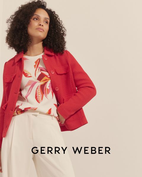 Une femme aux cheveux bouclés porte une veste texturée rouge sur un haut fleuri coloré et un pantalon couleur crème. L'arrière-plan est simple et le texte « Gerry Weber » est visible en bas.