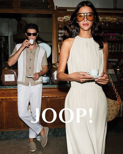 Homme et femme en tenue d'été élégante dans un café. L'homme porte une chemise beige et tient une tasse, tandis que la femme en robe claire tient une soucoupe. Ils portent tous les deux des lunettes de soleil. "JOOP !" est clairement visible.