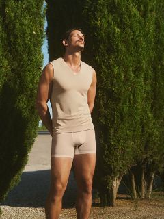 Une femme vêtue d'une robe rouge et de lunettes de soleil en forme de cœur est assise sur une chaise blanche, entourée de fleurs colorées, notamment des roses, des marguerites et des lys. L'environnement semble être un espace extérieur nocturne.