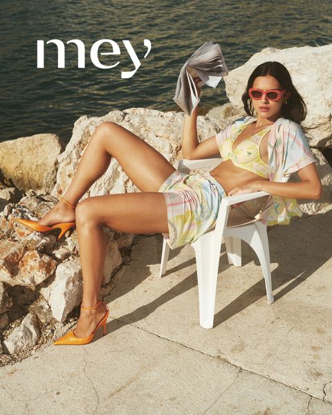 Un homme en caleçon boxer noir et une femme en débardeur blanc et sous-vêtements se tiennent côte à côte à l'extérieur, appuyés contre une balustrade, avec la mer et le ciel nuageux en arrière-plan. Le mot "mey" apparaît en bas.