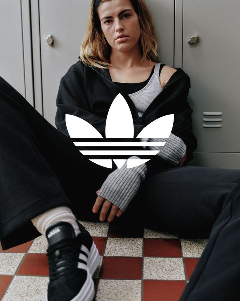 L'image montre le logo Adidas trèfle blanc avec trois feuilles et trois bandes horizontales, centré sur un fond bleu uni.