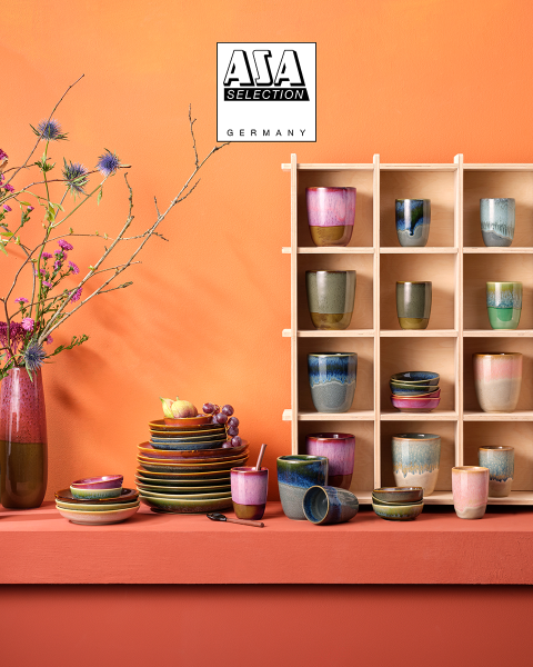 Des carafes couleur ambre avec des verres assortis, remplies d'un liquide brun, sont posées sur un plateau doré devant un fond texturé gris et atmosphérique. En haut, le logo d'ASA Selection Germany est représenté.