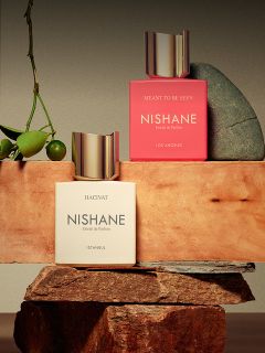 Un flacon du parfum "Hundred Silent Ways" de Nishane avec un bouchon doré qui se reflète en bas, et un arrière-plan rouge et noir flou.