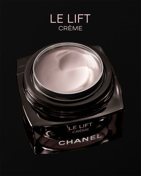 Une femme à la peau éclatante pose à côté de deux produits Chanel Les Beiges Correcteur, portant des bijoux en argent sur un fond beige délicat.