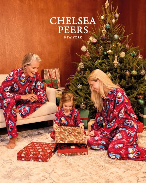 Trois personnes en pyjama à motifs sont assises sur un tapis devant un canapé jaune et jouent à un jeu. Le sol est décoré d'un tapis à motifs et une plante est visible à l'arrière-plan. Elles sourient et s'occupent des figurines.
