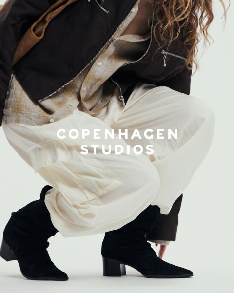 Une personne portant des bottes à lacets noires épaisses et un pantalon foncé se tient sur une surface blanche. Une partie de l'image est obscurcie par du fil rose et beige flou. Le texte "Copenhagen Studios" apparaît au-dessus de la photo.