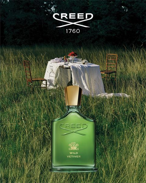 Un flacon blanc de parfum Creed Silver Mountain Water repose dans la neige, avec des sommets enneigés en arrière-plan sous un ciel bleu.