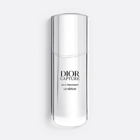 Un flacon Dior Capture OX-C Treatment Le Sérum, fin et translucide. Le flacon est haut et incurvé, avec un design minimaliste et un texte noir sur le devant. Sur un fond gris clair.