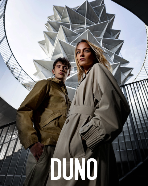 Une personne se tient de profil, portant une veste jaune clair et une jupe blanche, la tête inclinée vers l'arrière et les yeux fermés. Elle se trouve dans un environnement extérieur avec de grands cactus et des palmiers. Le mot "DUNO" apparaît verticalement sur le côté gauche de l'image.