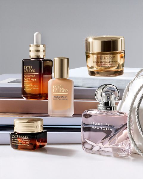 Une femme aux cheveux longs pose avec un flacon d'Estée Lauder Advanced Night Repair au premier plan. En arrière-plan, on aperçoit un paysage urbain nocturne. Un texte allemand décrit les avantages du produit de soin de la peau.