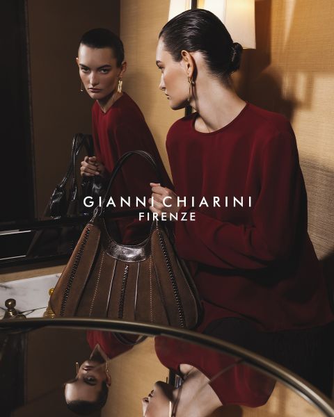 Personne portant un long trench-coat noir en cuir et des lunettes de soleil, tenant un petit sac à motif léopard. Le fond est gris, avec le texte "GIANNI CHIARINI FIRENZE" en blanc au-dessus de l'image.