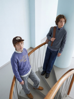 Deux garçons en jeans et chemises en jean posent ensemble. L'un est assis sur un tabouret, les mains sur les genoux et une écharpe autour du cou, tandis que l'autre, le bras posé sur le tabouret, porte un bonnet.