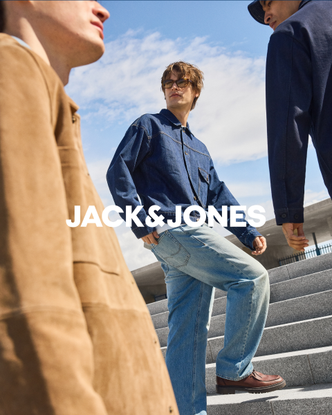 Deux hommes en tenue de jeans sont assis devant un fond simple. L'homme de devant porte sa main à sa bouche, tandis que l'autre est assis derrière lui. Au centre, on peut lire le texte "JACK & JONES".