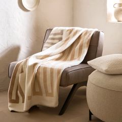 Une chaise moderne et ronde avec un coussin moelleux se trouve à côté de rideaux transparents à motifs, près d'une fenêtre. Un coussin assorti repose sur le plancher en bois et une lumière douce filtre à travers la fenêtre, créant une atmosphère chaleureuse.