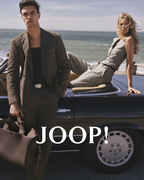 Homme et femme en tenue d'été élégante dans un café. L'homme porte une chemise beige et tient une tasse, tandis que la femme en robe claire tient une soucoupe. Ils portent tous les deux des lunettes de soleil. "JOOP !" est clairement visible.