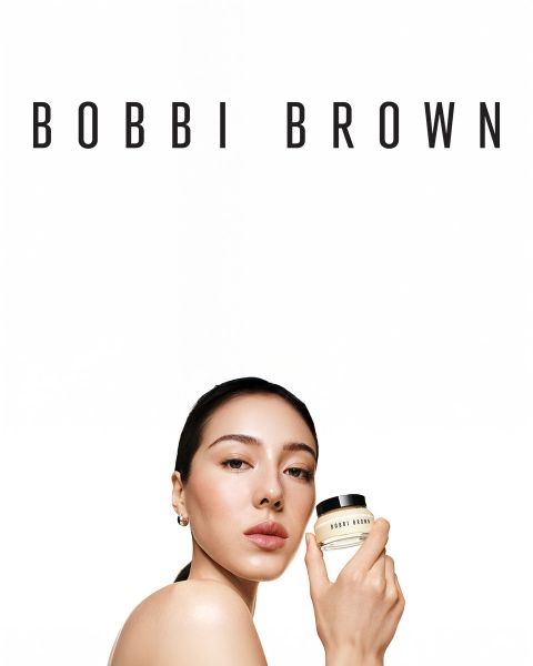 Une sélection de crayons fard à paupières crème longue tenue de Bobbi Brown dans différentes teintes, présentés horizontalement sur une surface texturée. Chaque crayon est ouvert, révélant les couleurs crémeuses. Le nom de la marque est visible sur les capuchons.