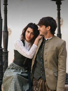 Une femme et un homme en costume traditionnel bavarois sont assis ensemble en plein air, souriant et se regardant.