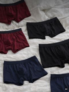 Six paires de boxers pour hommes en noir, bordeaux et bleu marine sont étalées sur un fond en tissu blanc.