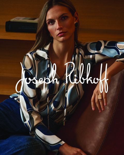 Une femme en chemisier à motifs et jean est assise sur un canapé en cuir ; sur l'image est écrit « Joseph Ribkoff » en lettres blanches.