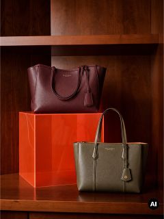 Deux sacs fourre-tout en cuir, un bordeaux et un vert olive, présentés sur des étagères en bois avec un bloc acrylique orange.