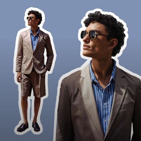 Homme portant des lunettes de soleil, un blazer beige, une chemise à rayures bleues et un short beige, se tenant avec assurance devant un arrière-plan en dégradé de brun.