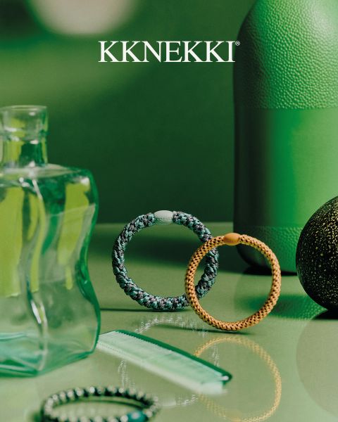 Une personne en pull bleu marine et jean tient une brosse à cheveux bleue derrière son dos et porte des bracelets de perles turquoise. Au-dessus, le logo "KKNEKKI".