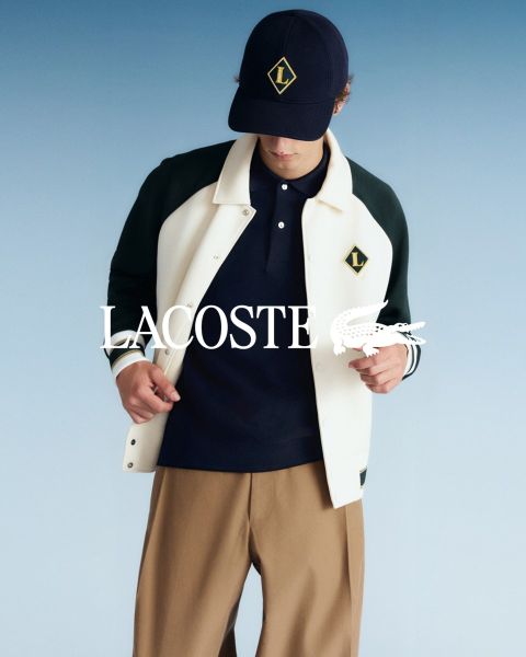 Quatre mannequins posent en extérieur, vêtus de tenues Lacoste, devant un ciel bleu. De gauche à droite : une personne en trench-coat, une personne en pull et pantalon, une personne en gilet et jupe, et une personne en survêtement. Le logo Lacoste se trouve en bas.