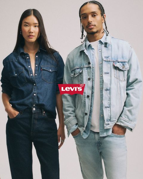 Un homme et une femme s'embrassent devant un fond patchwork bleu, tous deux vêtus de vestes et de jeans en denim. Un logo Levi's rouge est bien visible au-dessus d'eux.