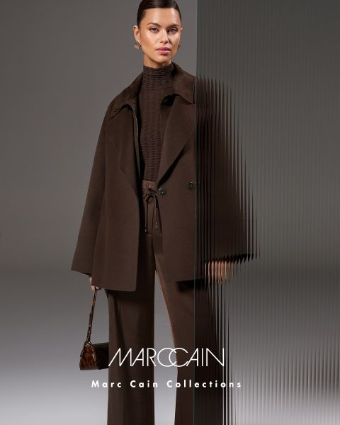 Une femme pose avec assurance dans une veste en cuir bordeaux et une jupe avec une grosse écharpe bordeaux texturée. Un ciel sombre est visible en arrière-plan, et le nom de la marque "Marc Cain" est visible en bas.