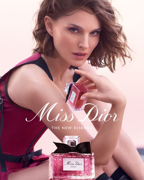 Un flacon de parfum Dior doré, entouré de papillons dorés flottants, d'un ruban rose et de délicates fleurs blanches avec le texte "DIOR Because I Adore You".