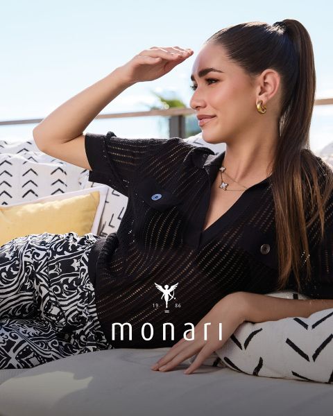 Une femme souriante portant un manteau beige, une chemise rayée, un jean bleu et une écharpe claire se tient à l'extérieur devant un grand bâtiment. Le logo Monari est visible en bas de l'image.