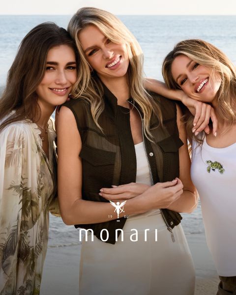 Une femme souriante portant un manteau beige, une chemise rayée, un jean bleu et une écharpe claire se tient à l'extérieur devant un grand bâtiment. Le logo Monari est visible en bas de l'image.