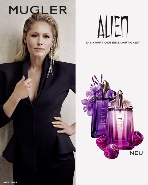 Une femme à la peau foncée et éclatante et aux cheveux noirs lisses pose devant un fond violet. Devant elle se trouvent deux flacons de parfum Alien de Mugler. Le texte indique « MUGLER » et « ALIEN EXTRA INTENSE LES FRAGRANCES RECHARGEABLES ».