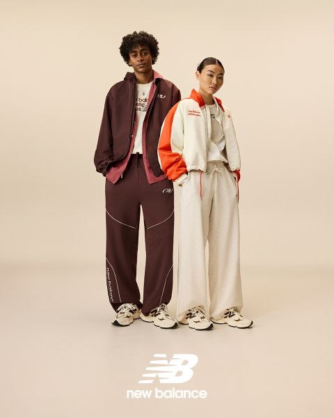 Un homme et une femme posent devant des enseignes au néon. L'homme porte un survêtement beige, la femme une salopette en jean. Ils portent tous les deux des baskets New Balance. La scène est éclairée par diverses lumières néon bleues et rouges.
