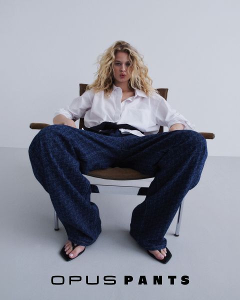 Personne en chemise blanche décontractée et blue-jeans, les mains sur les hanches. En bas, le texte "Opus Pants". Les cheveux sont légèrement ébouriffés par le vent, fond blanc.