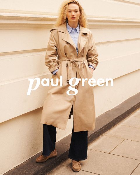 Une personne aux longs cheveux roux, portant des lunettes de soleil, un haut vert clair, un pantalon beige et des baskets bleues est assise sur un terrain rocailleux sous un ciel bleu. Les mots "Paul Green" sont superposés à l'image.