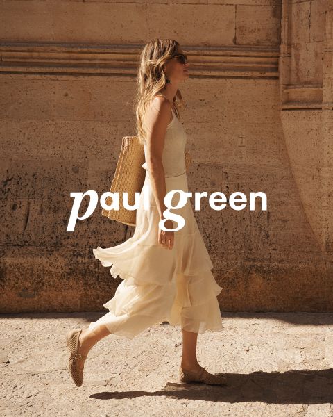 Une personne aux longs cheveux roux, portant des lunettes de soleil, un haut vert clair, un pantalon beige et des baskets bleues est assise sur un terrain rocailleux sous un ciel bleu. Les mots "Paul Green" sont superposés à l'image.