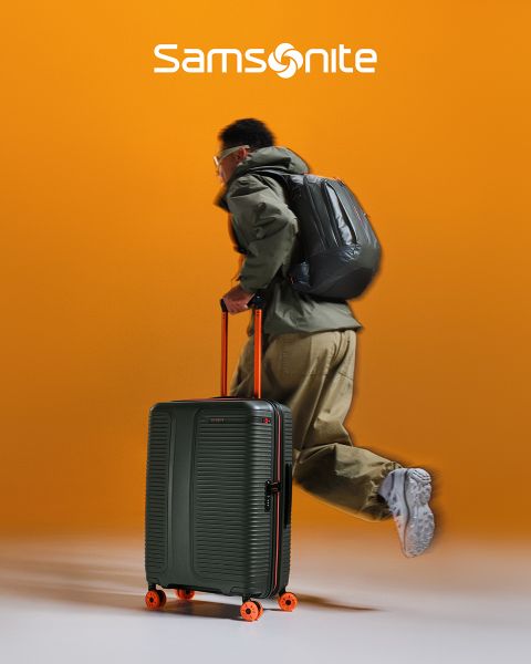 Valise Samsonite vert clair avec un motif texturé et quatre roulettes. La poignée est extensible. Le grand logo « Samsonite » est étalé en travers de la valise. L'arrière-plan présente un motif ondulé vert et blanc.