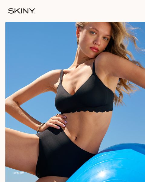 Une femme aux cheveux tressés ferme un soutien-gorge rose clair à fermeture frontale devant un fond rouge foncé. Le mot « SKINY » apparaît en bas de l'image.