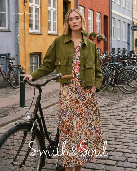 Une femme en chemise rose et cardigan avec un pantalon blanc pose devant un fond blanc. Le texte indique « Smith & Soul » en bas.