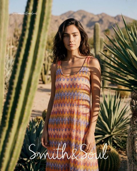 Une femme en chemise rose et cardigan avec un pantalon blanc pose devant un fond blanc. Le texte indique « Smith & Soul » en bas.