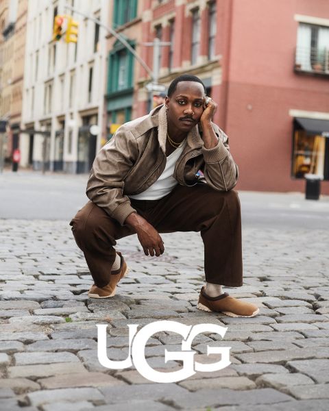 Une paire de bottes UGG en daim marron avec une doublure intérieure moelleuse, posée sur une surface grise. Le logo UGG est bien visible en bas de l'image.